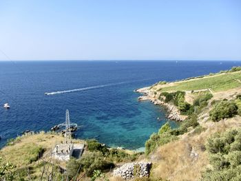 High angle view of beach in bay against clear sky, with transmission tower and a boat 