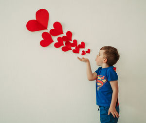 Full length of boy holding heart shape against wall
