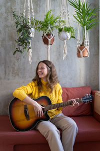 Full length of woman playing guitar on sofa