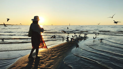 Rear view of silhouette woman standing on beach against sky during sunset