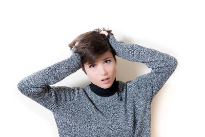 Portrait of sad young woman with hand in hair against white wall