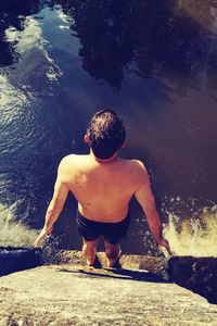 Rear view of shirtless man standing on wall by river