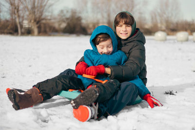 Full length of boy sitting on snow covered field