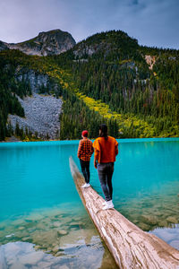 Rear view of couple standing on wood in lake against mountains and sky