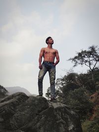 Low angle view of shirtless man standing on rock against sky
