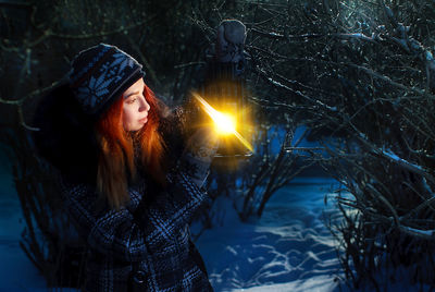 Pretty redhead girl holding lantern in winter forest