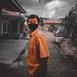 Portrait of young man standing on street against sky