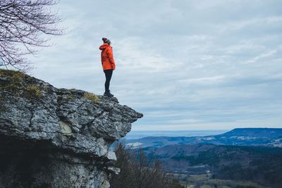 Side view of mature woman standing on rock against cloudy sky