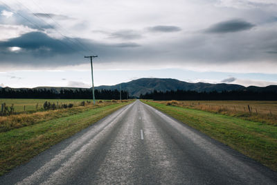 Country road amidst field against sky