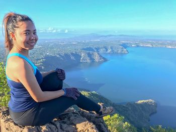 Young woman sitting on rock by sea against mountains