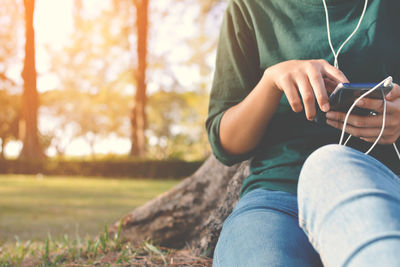 Midsection of woman using phone while sitting on field