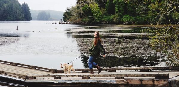 Woman with dog walking on pier over lake