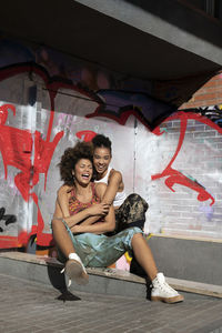 Happy friends embracing in front of graffiti wall on sunny day