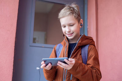 A cute boy is standing with a backpack and a phone with headphones