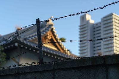 Low angle view of barb wires on surrounding wall against buildings