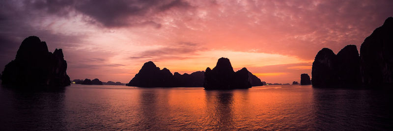 Silhouette rocks by sea against romantic sky