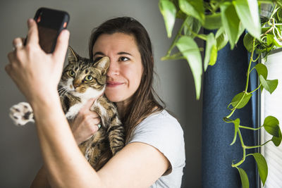 Woman indoors at home taking selfies with her cat by the window