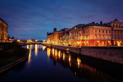 Illuminated buildings by river against sky at night