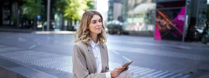 Portrait of young woman using mobile phone in city