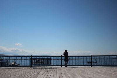 Rear view of man looking at pier on sea against sky