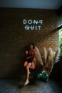 Full length of woman sitting against wall