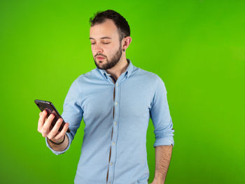 Young man using mobile phone against green background