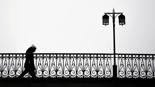 Silhouette man standing by street light against clear sky