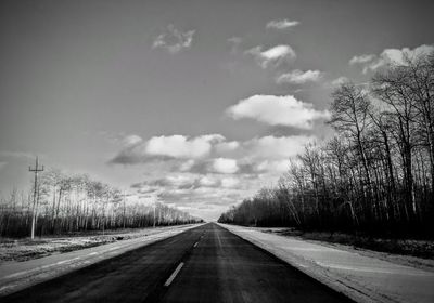 Empty road amidst trees against sky