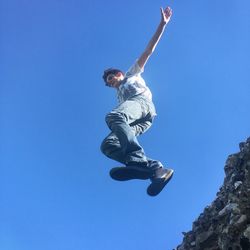 Low angle view of boy jumping from retaining wall against clear blue sky