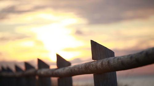 Close-up of metal fence against orange sky