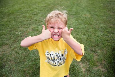 Silly blonde boy squishes face with two thumbs up at school field day