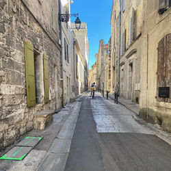 Rear view of man riding bicycle on footpath amidst buildings