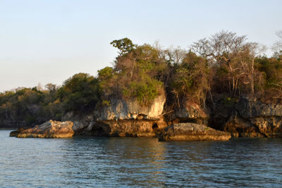 Scenic view of rocks by sea against clear sky