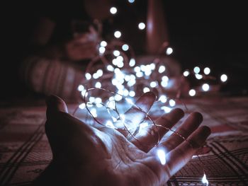 Cropped hand holding illuminated lights on bed at home