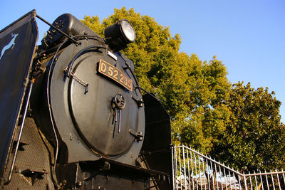 Low angle view of train by trees against sky