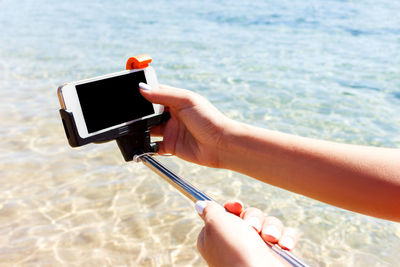 Cropped hand adjusting smart phone on monopod at beach