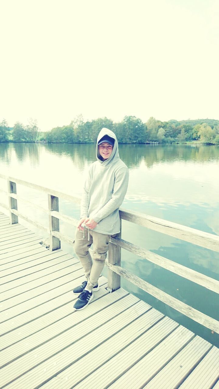 water, casual clothing, sitting, lake, leisure activity, full length, lifestyles, clear sky, reflection, sunlight, pier, relaxation, day, nature, standing water, person, looking at camera, sky, tranquility, outdoors, tranquil scene, scenics, young adult, beauty in nature