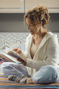 Young woman using mobile phone while sitting on bed at home