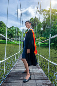 Portrait of young woman wearing graduation gown standing on footpath