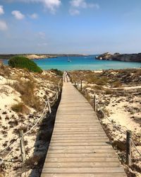 Boardwalk leading towards sea against sky