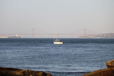 Yacht over tagus river against 25 de abril bridge