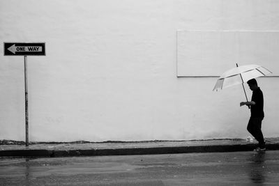 Man walking under umbrella against wall during rainfall