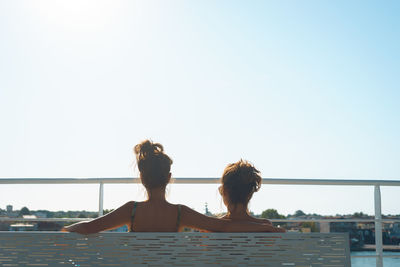 Rear view of woman relaxing on railing against clear sky