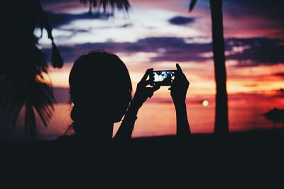 Rear view of silhouette man photographing at sunset