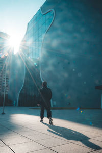 Rear view of man walking on sidewalk in city against bright sky