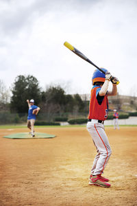 Side view of boy playing baseball with coach on field against sky