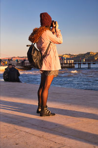 Woman standing at beach against sky during sunset