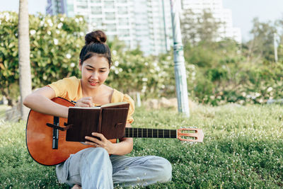 Smiling woman making note while sitting with guitar at park