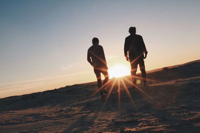 Silhouette men walking on landscape against sky during sunset