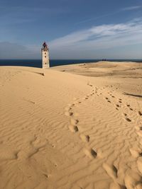 Lighthouse on sand dunes at beach by sea against sky